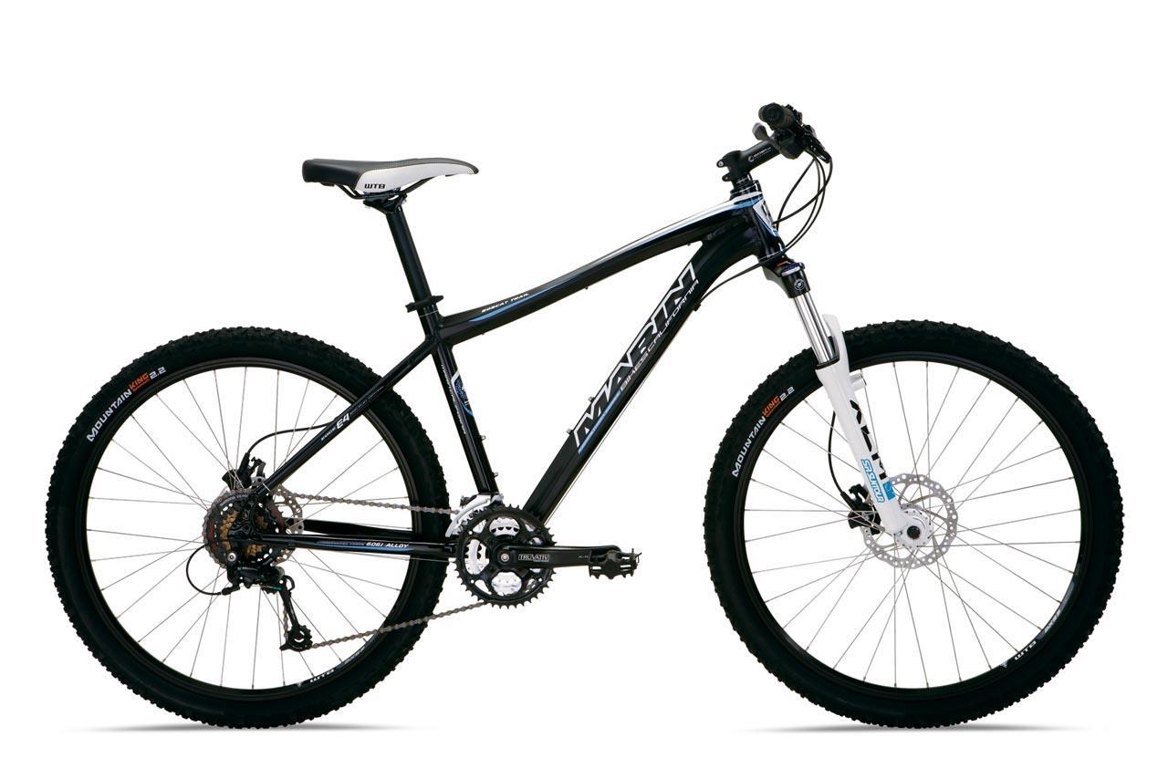Marin Bobcat Trail: Mountain bike with a black and white frame, featuring thick tires suitable for off-road terrain, a front suspension fork, and a geared drivetrain. The bike is shown from the side against a plain background.