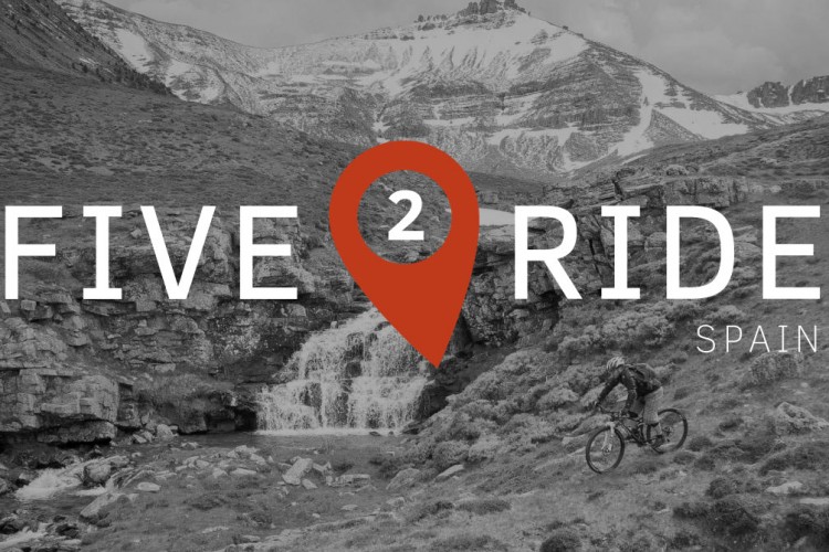 A scenic landscape featuring a cyclist riding through a grassy area with a waterfall in the background. Snow-capped mountains rise in the distance. Overlayed text reads "FIVE 2 RIDE SPAIN," with a location marker graphic. The image has a monochrome effect except for the text and marker.