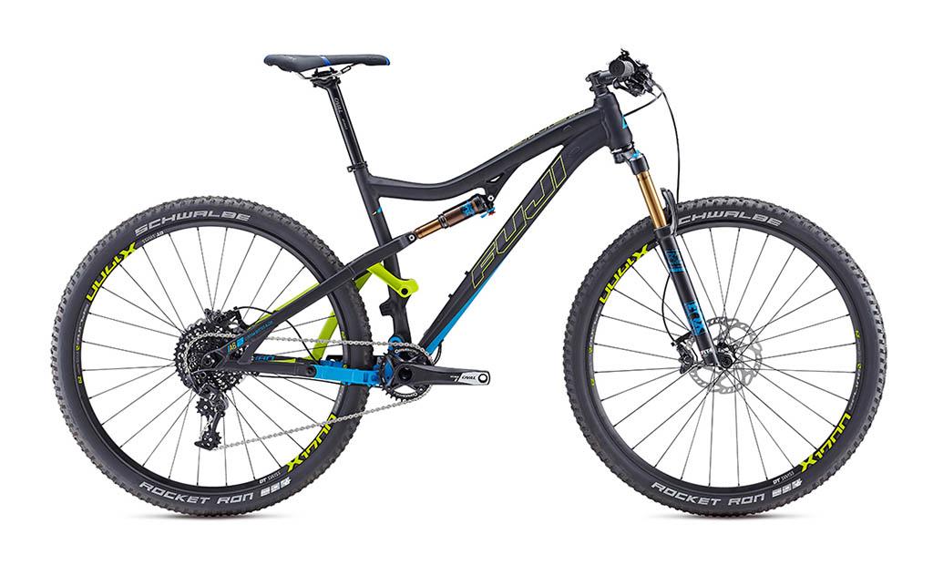 Fuji Rakan: A modern mountain bike with a lightweight black frame featuring blue and green accents. It has large, knobby tires labeled "Schwalbe Rocket Ron" and a suspension fork, making it suitable for off-road trails. The bike is positioned sideways to showcase its design and components.