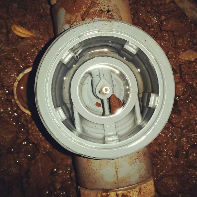 Close-up view of a gray valve or sprinkler head attached to a brown pipe, partially surrounded by mud and debris on the ground. Freedom Center mountain bike trail.