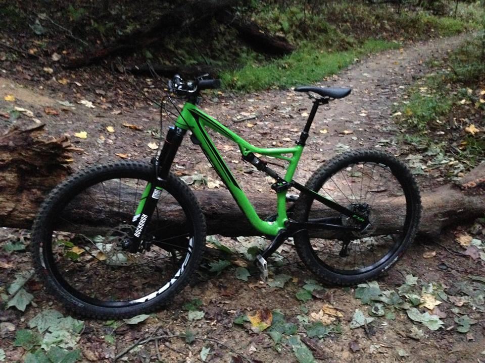 Specialized Stumpjumper FSR: A green mountain bike is parked next to a fallen log on a dirt trail, surrounded by scattered leaves and lush vegetation in a wooded area. The bike has thick tires and is positioned on a rugged path, indicating use in outdoor terrain.