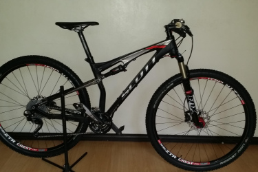 Scott 2013 Spark 960: A black and red mountain bike leaning on a stand against a light-colored wall. The bike features a full suspension design, thick tires, and disc brakes. The image showcases the bike's frame, wheels, and components clearly.