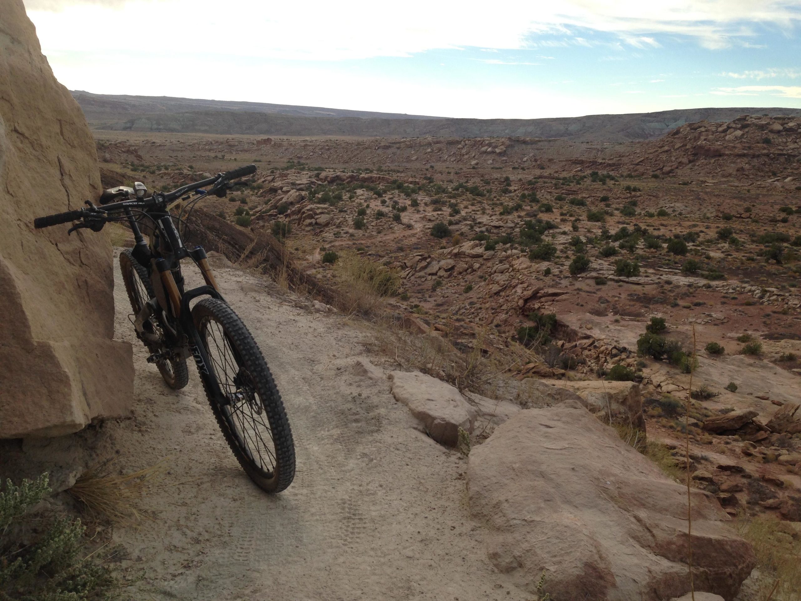 A mountain bike resting against a large rock on a rugged trail, with a vast landscape of rocky terrain and sparse vegetation in the background under a cloudy sky. Sovereign Single Track mountain bike trail.