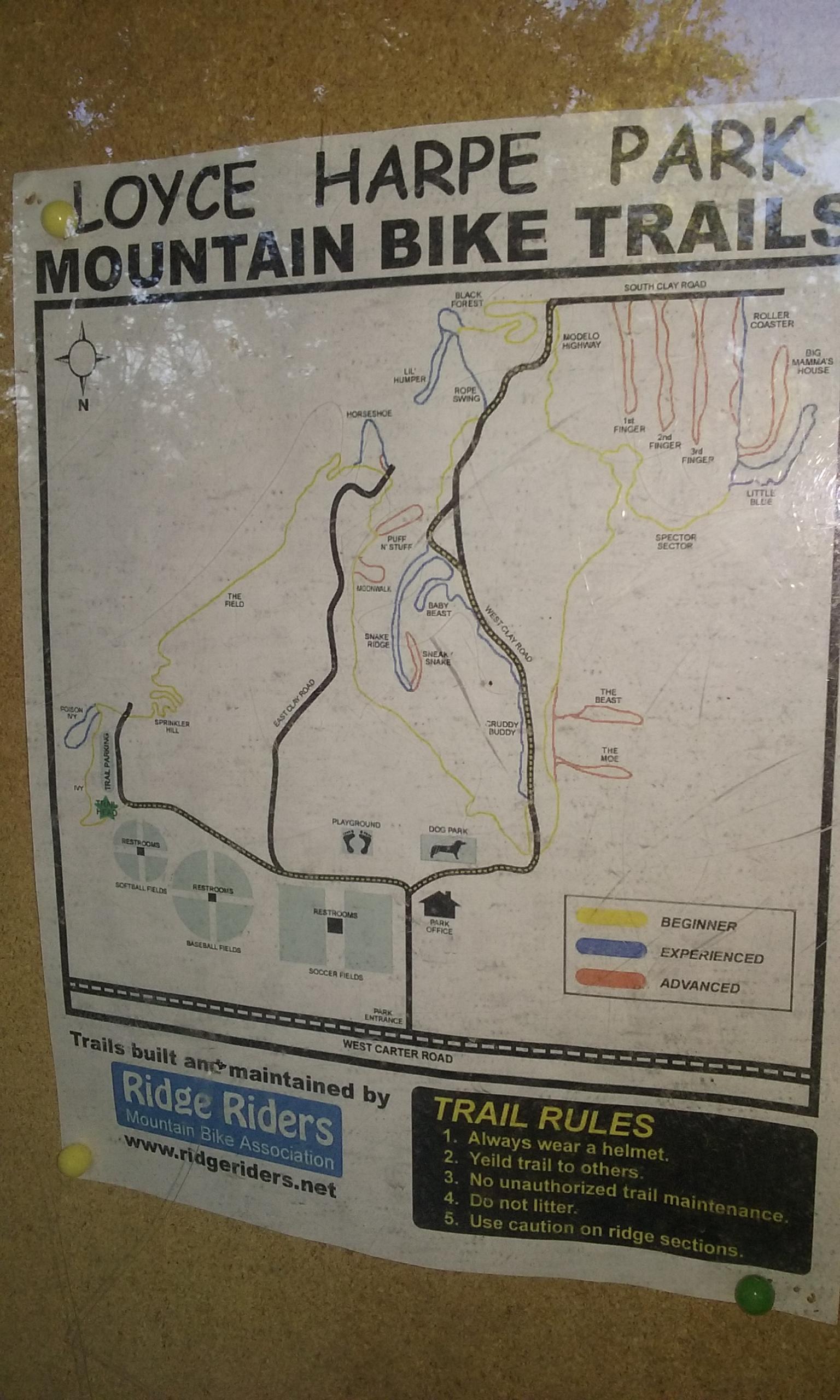 Map of Loyce Harpe Park Mountain Bike Trails, displaying various biking routes categorized by difficulty: beginner, experienced, and advanced. Key features include trail names, a compass rose, and park facilities like restrooms and playgrounds. The map also lists trail rules for safety. Loyce E. Harpe Park mountain bike trail.