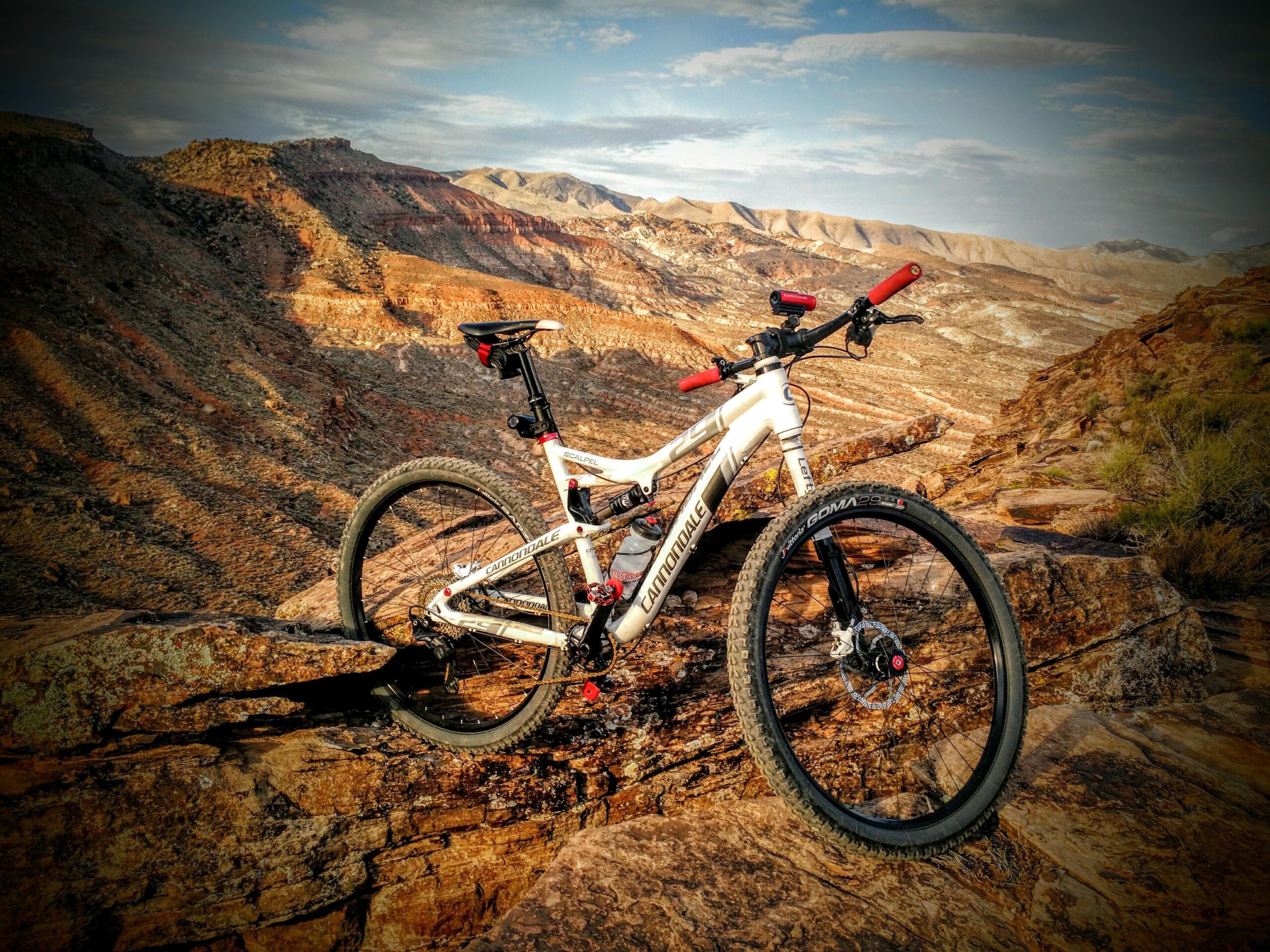 A mountain bike resting on a rocky outcrop with a scenic view of layered hills and mountains in the background, under a partly cloudy sky. Barrel Roll mountain bike trail.