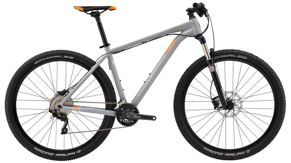 Marin Nail Trail 9.6: A lightweight mountain bike featuring a sleek gray frame with orange accents. The bike is equipped with front suspension, wide tires labeled "Schwalbe Racing Ralph," and a single-chainring drivetrain for efficient gear shifting. The handlebars are designed for a comfortable grip, making it suitable for off-road trails and cycling enthusiasts.