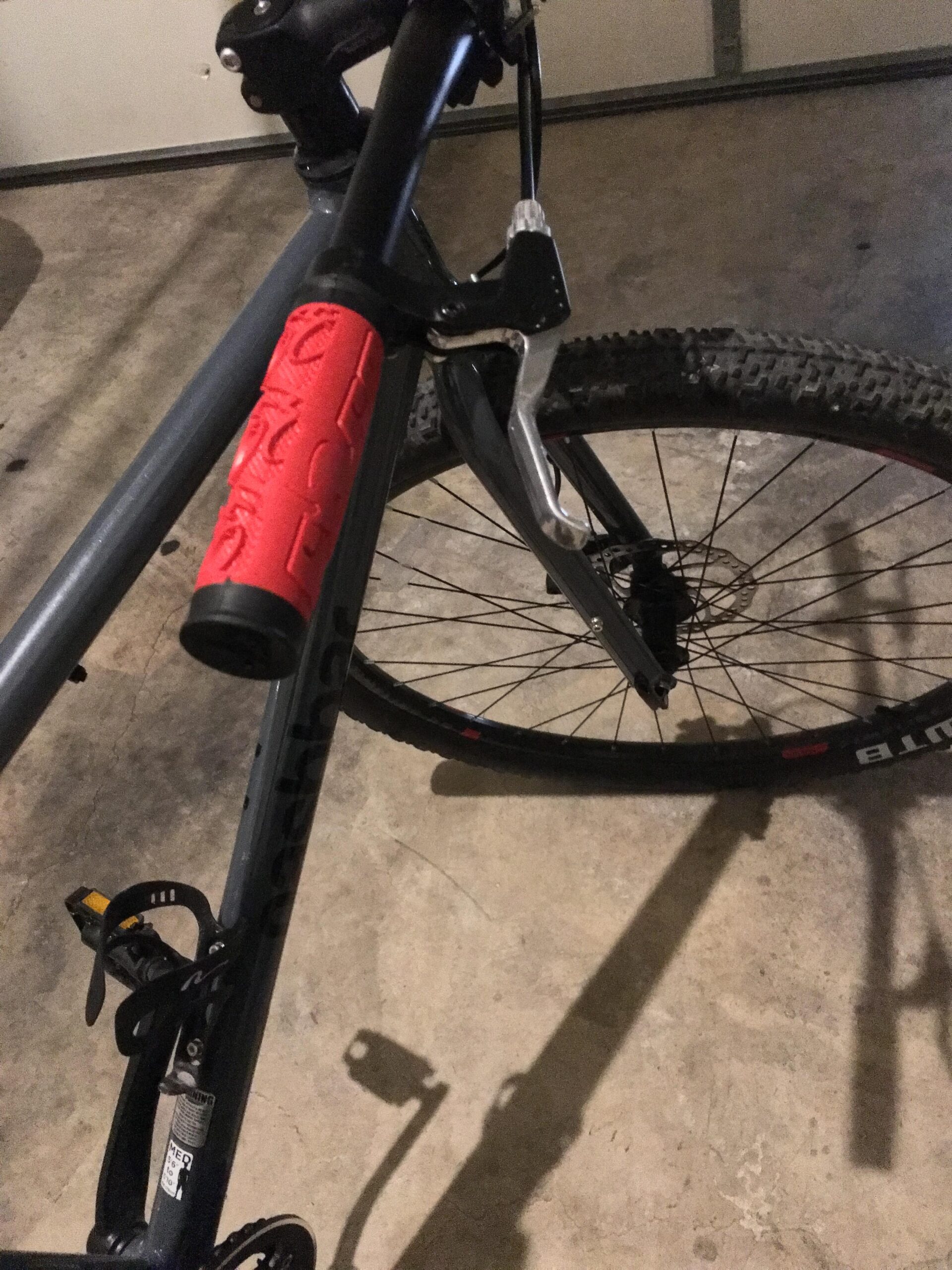 Nashbar SS 29er: Close-up view of a mountain bike showing the handlebars, brake lever, and a red textured grip. The bike is positioned on a concrete surface, with part of the rear wheel and pedal visible in the frame.