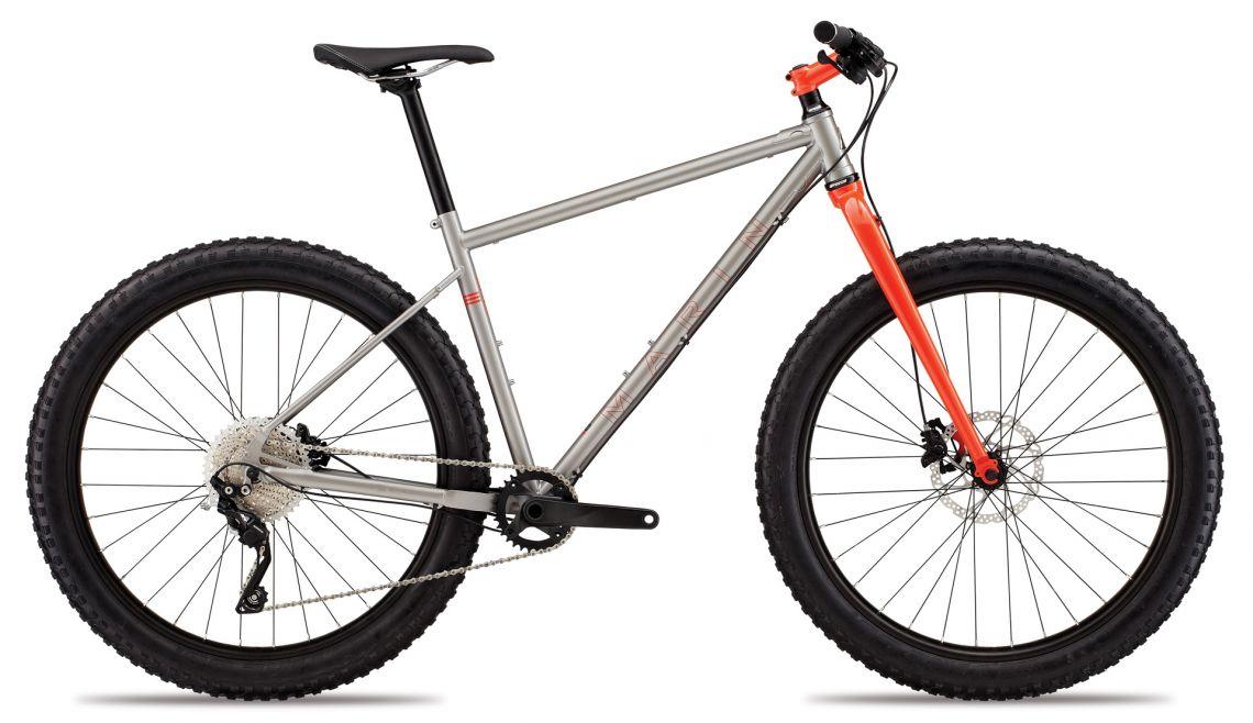 Marin Pine Mountain 27.5: A modern mountain bike with a sleek aluminum frame, featuring a silver body and an orange front fork. It has wide, textured tires for off-road traction, a single-speed drivetrain, and a comfortable saddle, designed for rugged terrain and outdoor adventures.