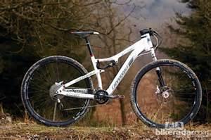 Cannondale Scalpel 29er 3: A white mountain bike parked on a gravel path with trees and a blurred natural landscape in the background.