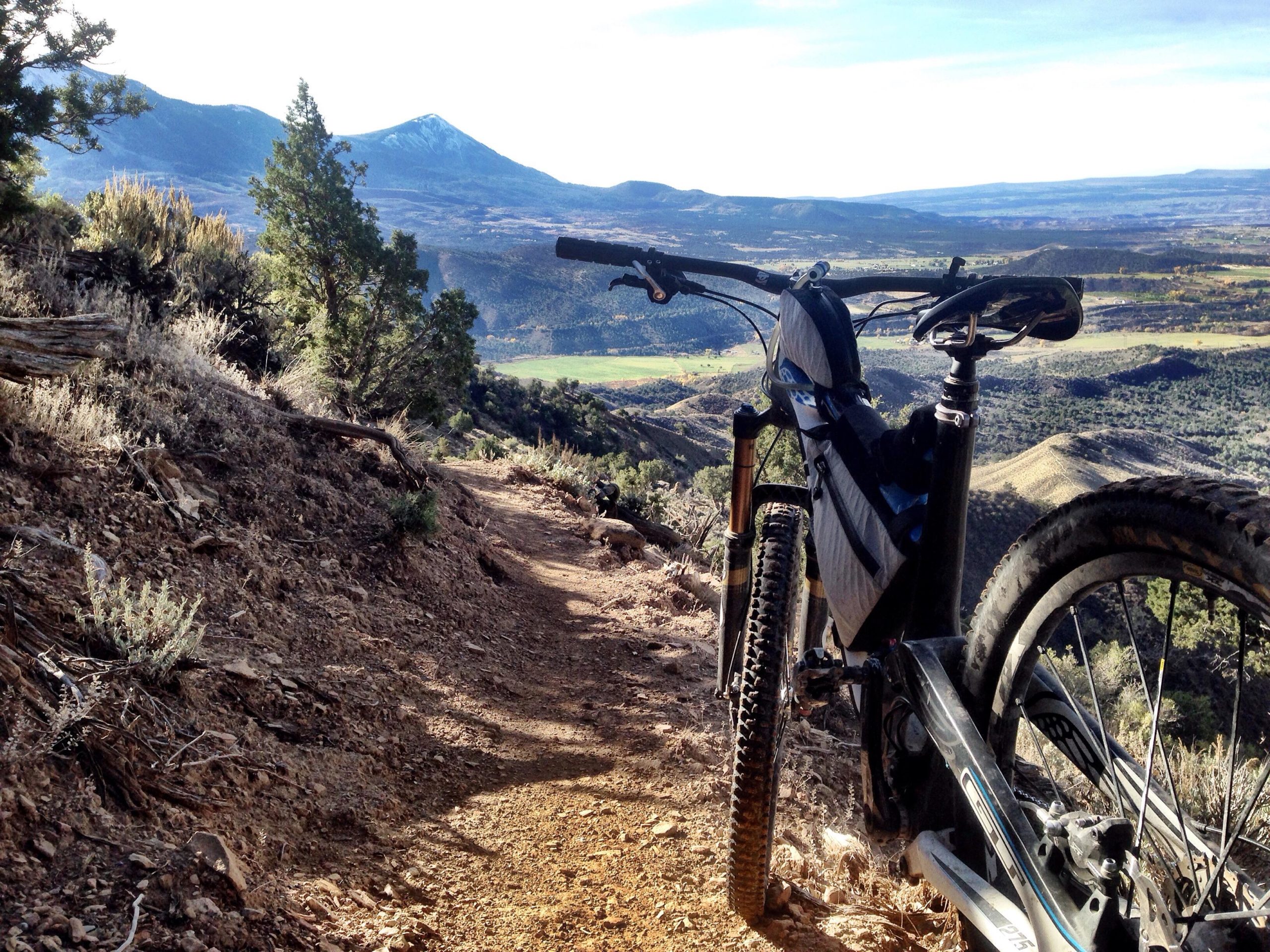 Mountain bike positioned on a rugged dirt trail overlooking a scenic valley and distant mountains under a clear sky. Jumbo Mountain mountain bike trail.