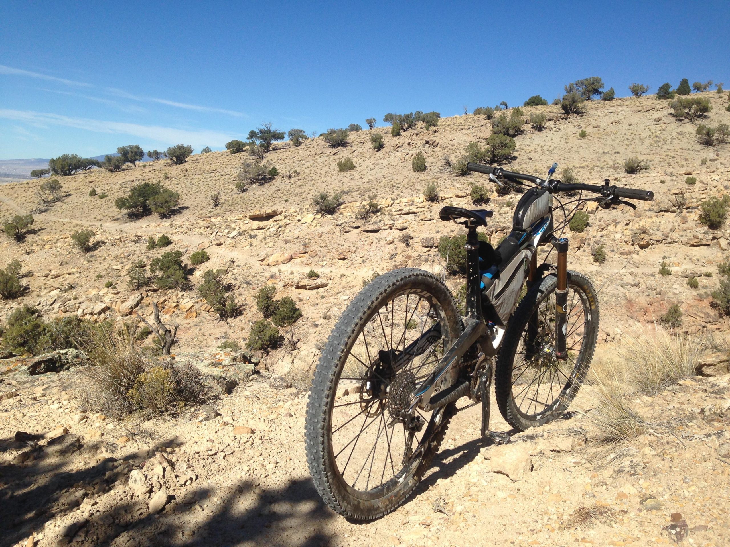 A mountain bike positioned on a rocky, arid terrain with sparse vegetation and a clear blue sky in the background. The scene captures a remote outdoor environment, ideal for cycling adventures. Sidewinder mountain bike trail.