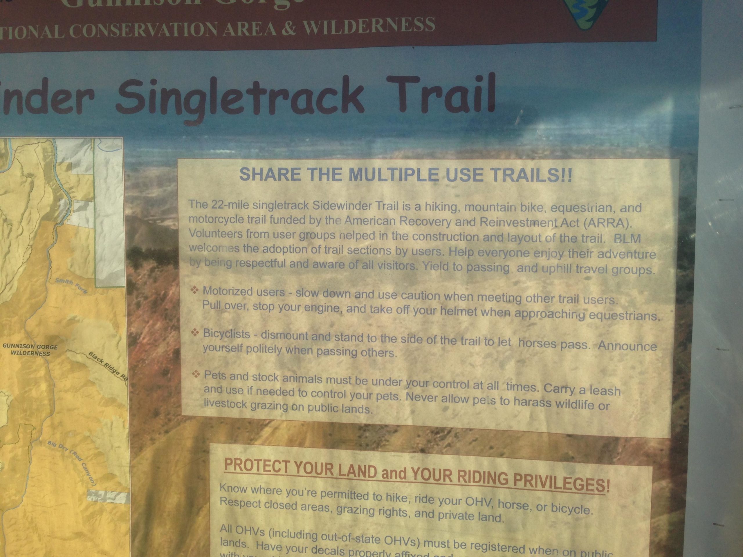 Alt text: A trail sign for the Sidewinder Singletrack Trail in Gunnison Gorge Wilderness, detailing guidelines for sharing the trail among hikers, bikers, equestrians, and motorized users, along with a map of the area. The sign emphasizes safety, respect for other trail users, and responsible pet management. Sidewinder mountain bike trail.