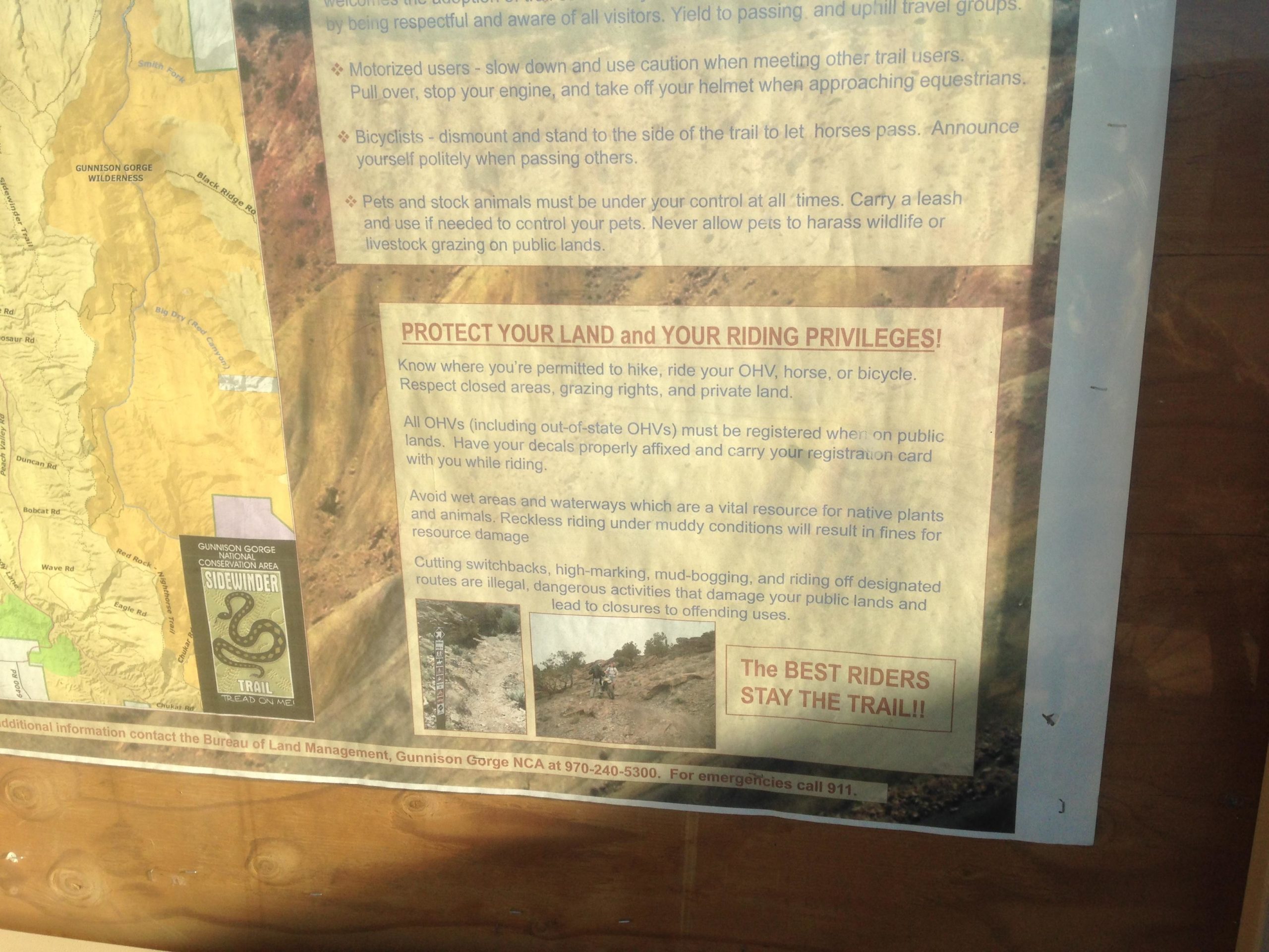 A close-up image of a trail information sign featuring guidelines for outdoor users in the Gunnison Gorge Wilderness area. The sign emphasizes the importance of respecting land and riding privileges, sharing safety tips for motorized users, bicyclists, and pets, as well as warnings against damaging the landscape. Clear instructions for staying on designated trails are highlighted to protect natural resources. Sidewinder mountain bike trail.