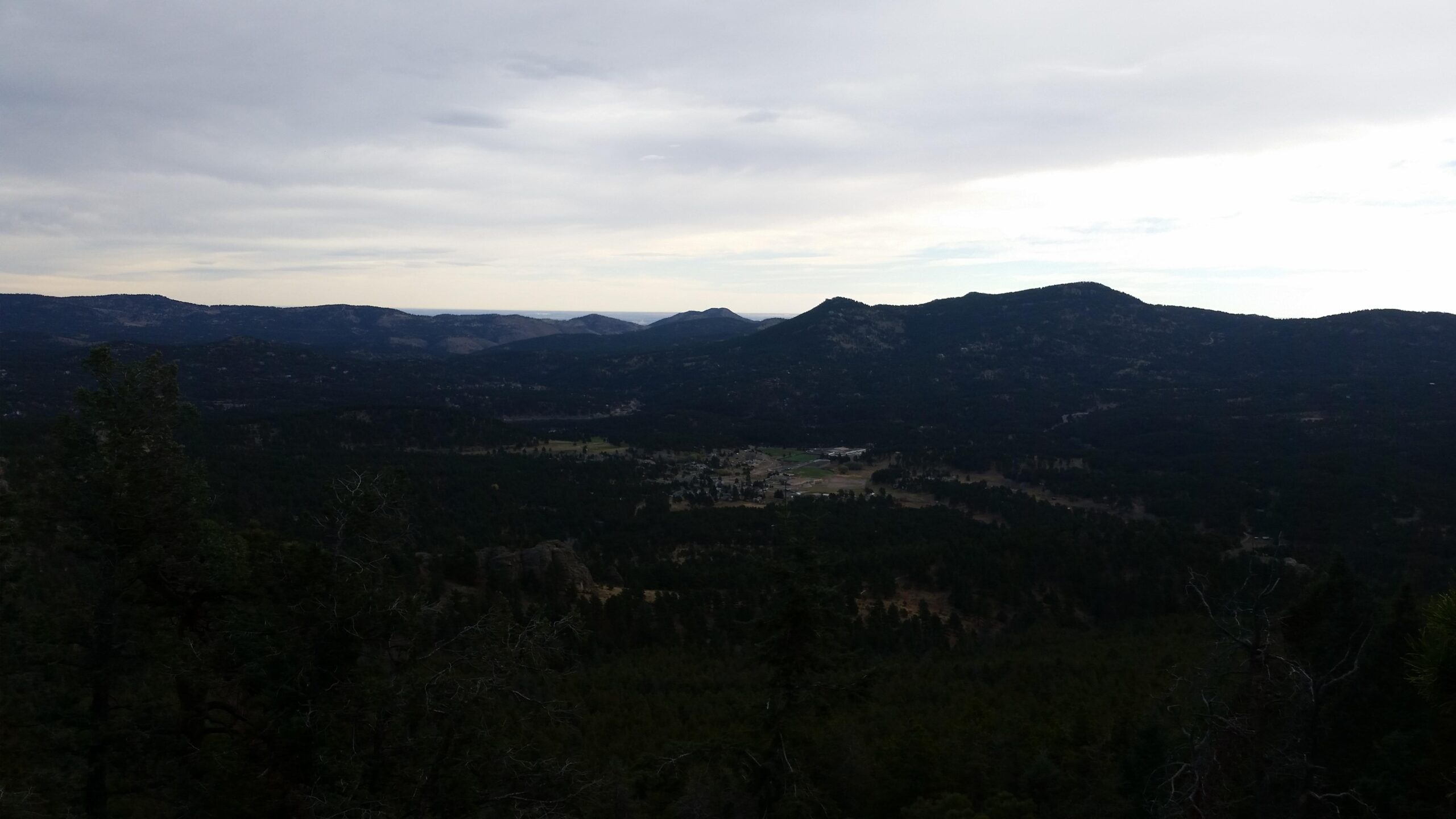 A panoramic view of a valley surrounded by mountains under a cloudy sky, showcasing a mix of greenery and open spaces. 3 Sisters / Alderfer mountain bike trail.