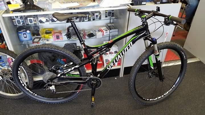 Specialized Epic FSR: A black and green Specialized mountain bike displayed in a bike shop, with a variety of cycling accessories visible in the background. The bike features knobby tires and a sleek frame design, suitable for off-road cycling.