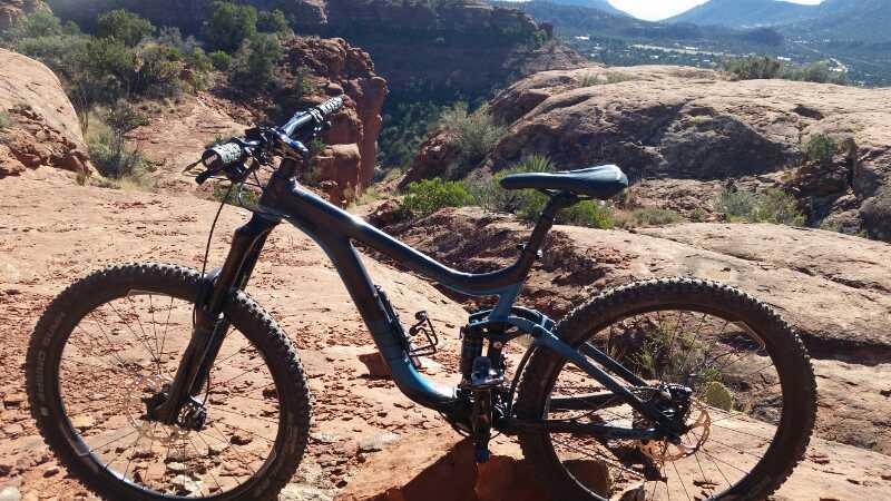 A mountain bike resting on rocky terrain, surrounded by scenic views of cliffs and greenery in a desert landscape under clear blue skies. Hiline mountain bike trail.