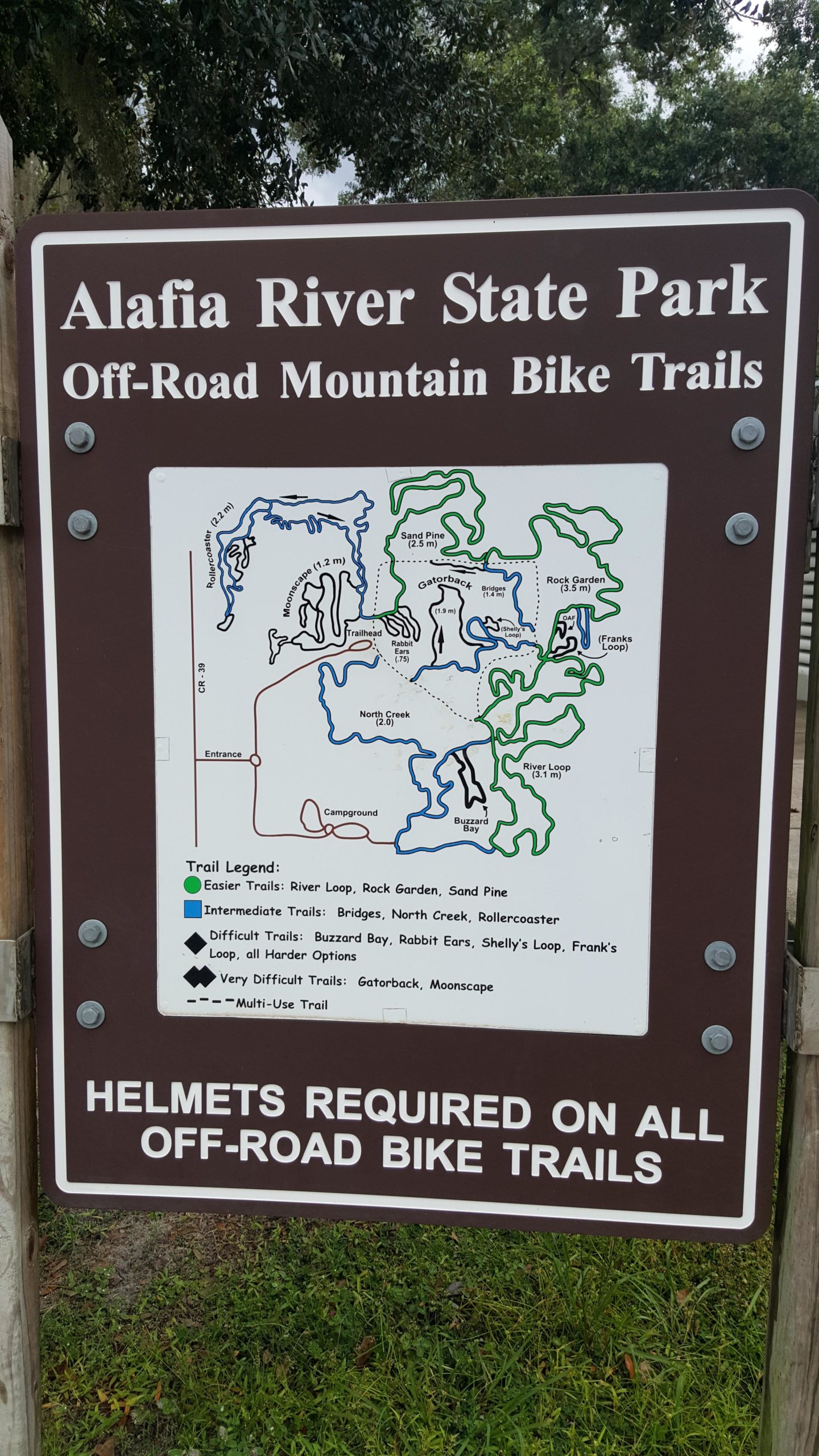 Sign at Alafia River State Park displaying a map of off-road mountain bike trails. The map includes trail names, difficulty levels, and distances, with a legend indicating easier, intermediate, and difficult trails. The sign also states that helmets are required on all off-road bike trails. Alafia River State Park mountain bike trail.