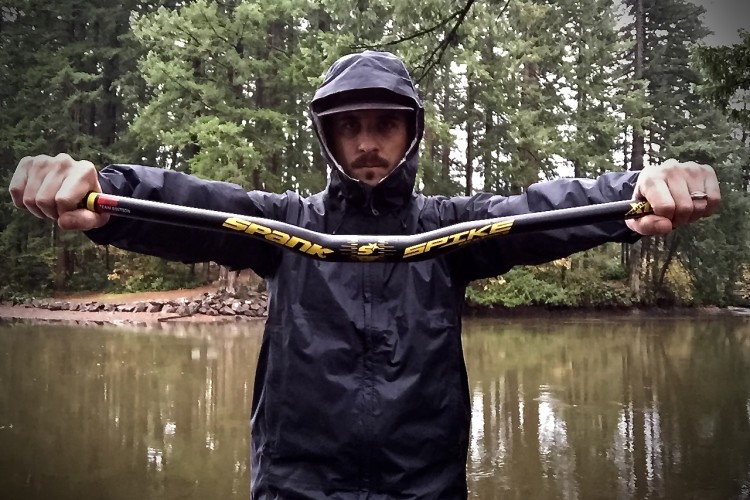 Person in a waterproof jacket holding a bicycle handlebar horizontally over a calm water surface, with trees in the background.