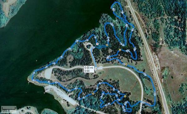 Map showing a trail system around a lake, with highlighted blue paths indicating different routes through wooded areas, alongside areas of open land. The map includes markers for points of interest and displays navigation details. Liminal Trail mountain bike trail.