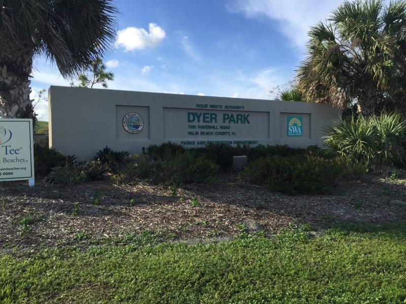 Sign for Dyer Park located on Manatee Road in Palm Beach County, Florida, displaying the name of the park and the Solid Waste Authority logo amidst landscaping and palm trees. Dyer Park mountain bike trail.