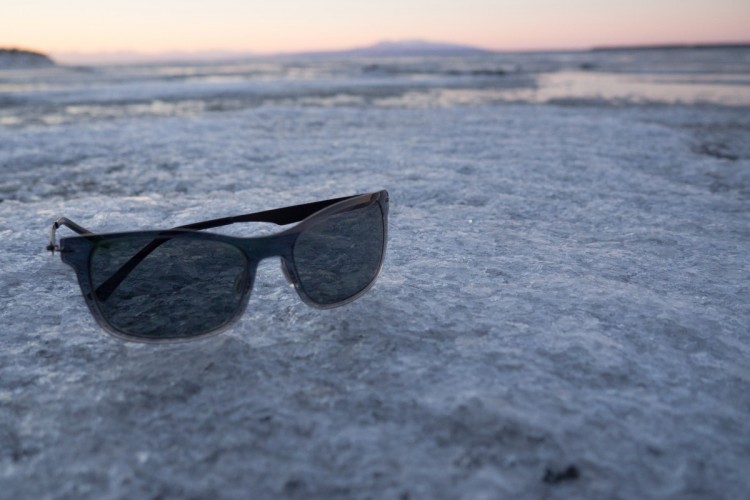 A pair of sunglasses resting on a frozen surface, with a serene landscape in the background at dusk, featuring soft pastel colors in the sky.