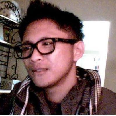 Specialized Stumpjumper: A young man with short hair and glasses, wearing a scarf and a jacket, is looking thoughtfully to the side. He appears to be seated in a room with soft lighting, with a glimpse of a door in the background.