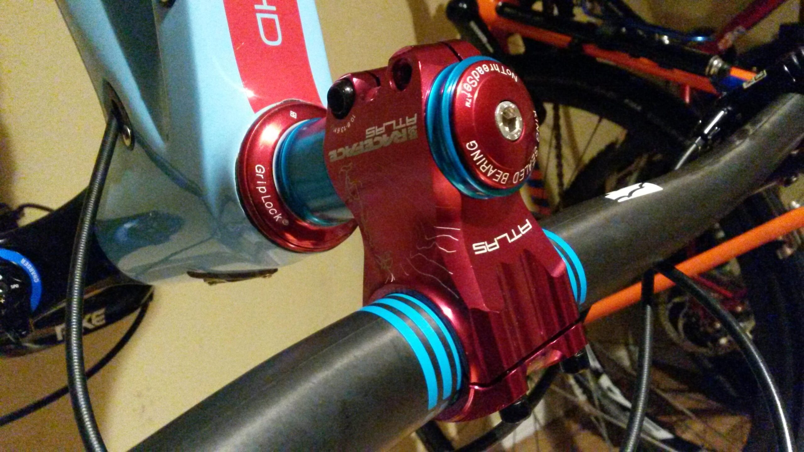 Ibis Mojo HD3: Close-up image of a brightly colored bicycle stem and handlebar, showcasing a red aluminum stem with blue accents and the text "Grip Lock." The stem is attached to a light blue bike frame, with cables and additional mountain bikes visible in the background.