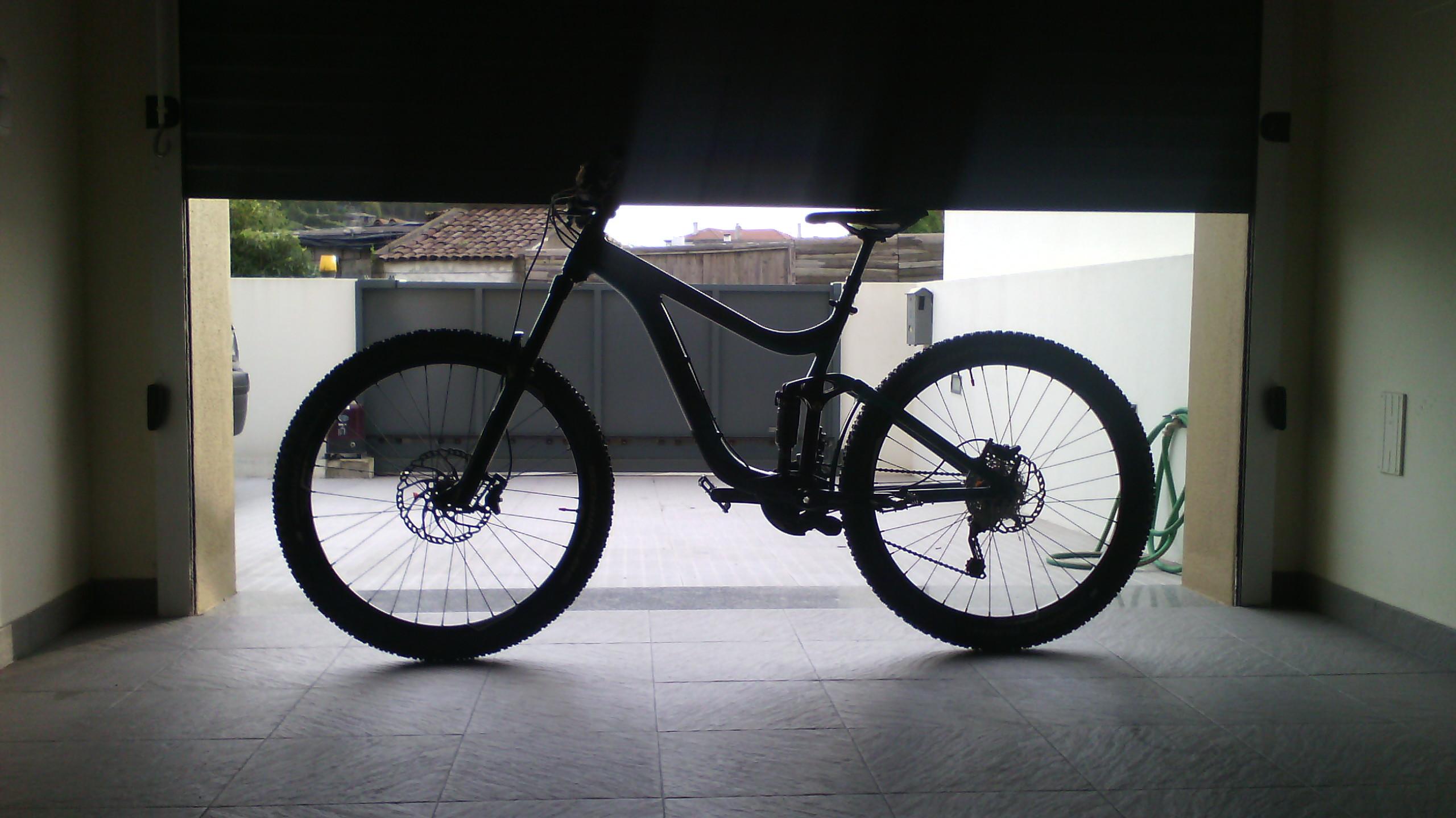 Giant Reign 2: A black mountain bike is positioned in silhouette against a partially open garage door, with a tiled floor and a glimpse of an outdoor area visible in the background.