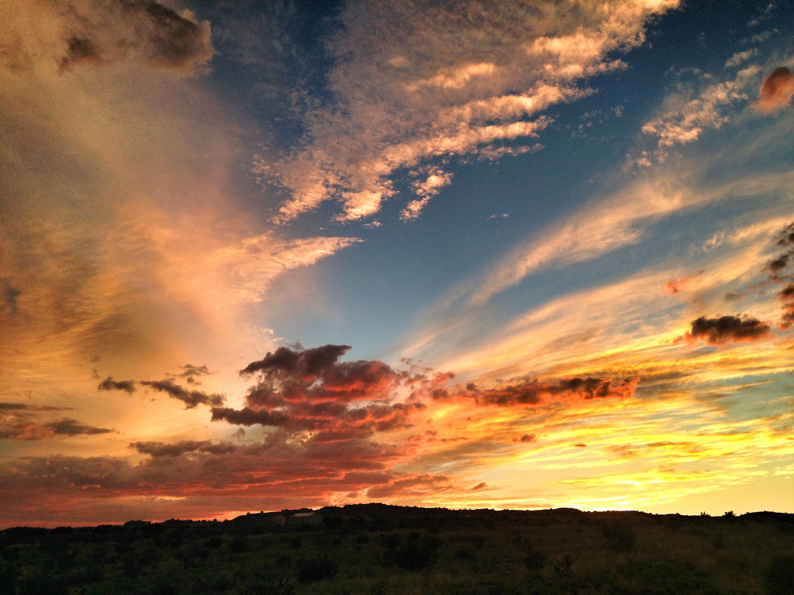 A vibrant sunset with dramatic clouds in shades of orange, pink, and blue, illuminating the sky above a silhouetted landscape. Parkway Fatbike trail mountain bike trail.