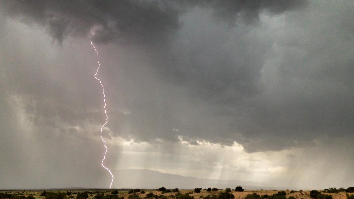 A dramatic lightning bolt striking down from dark, stormy clouds, with a desolate landscape and distant mountains beneath. The scene captures the intense atmosphere of an approaching storm. Parkway Fatbike trail mountain bike trail.