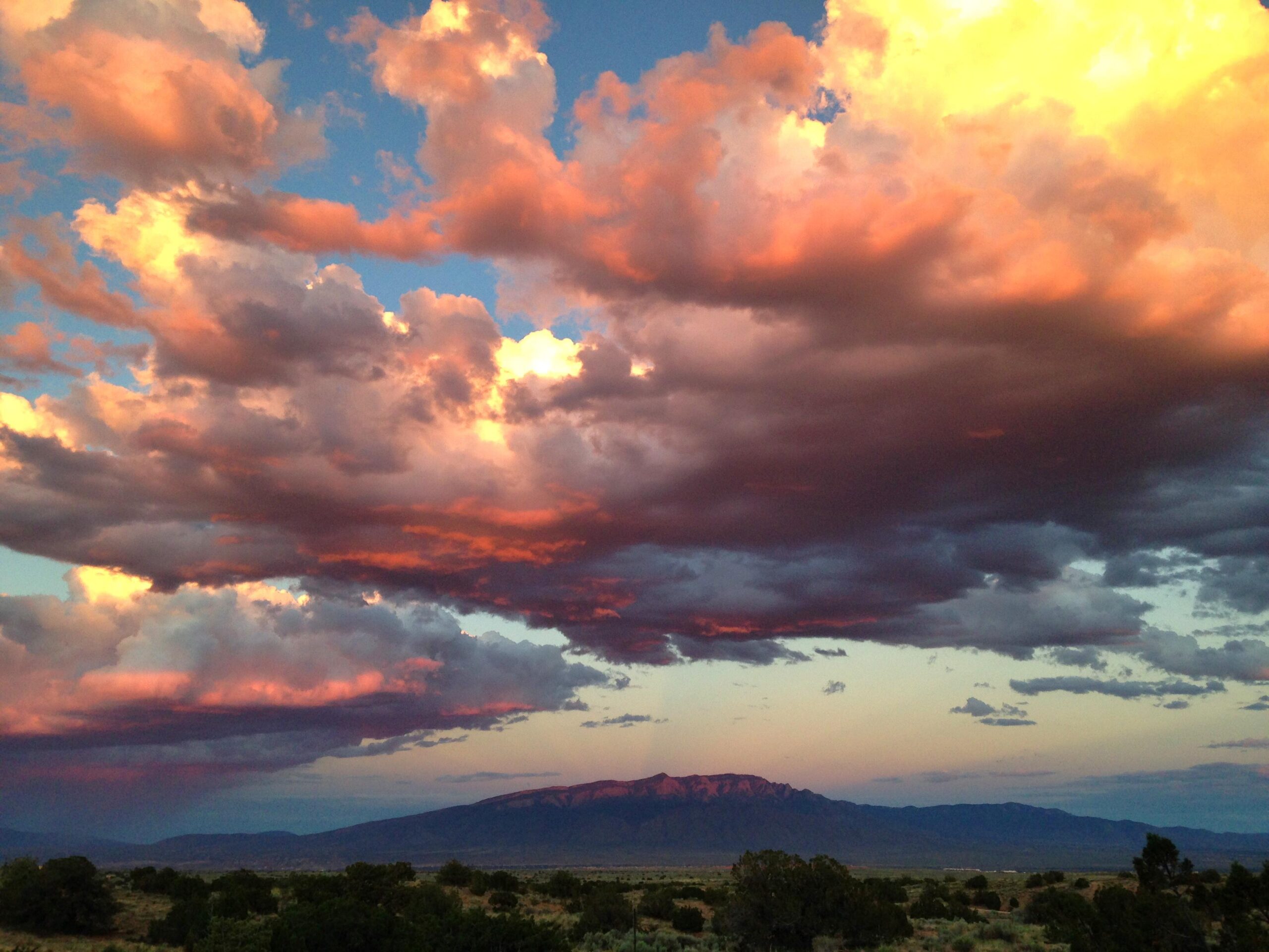 A vibrant sky at sunset filled with fluffy clouds displaying shades of pink, orange, and purple, above a distant mountain range and arid landscape. Parkway Fatbike trail mountain bike trail.