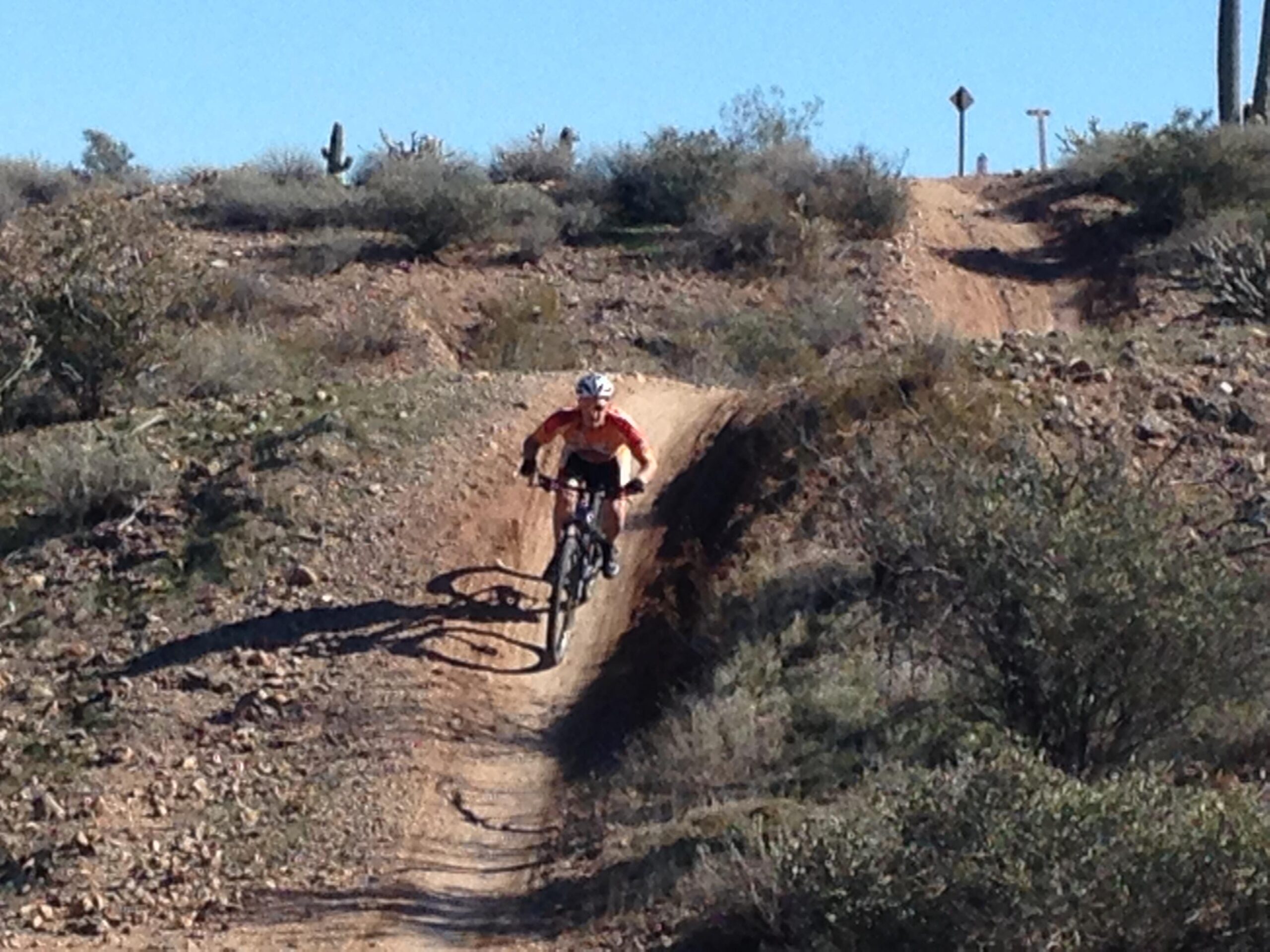 Giant Trance: A mountain biker navigating a rocky trail through a desert landscape, surrounded by sparse vegetation and cacti under a clear blue sky.