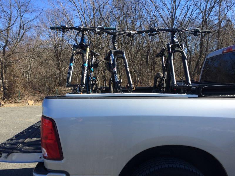 Bicycles secured in the bed of a silver pickup truck, with a backdrop of bare trees under a clear blue sky. Richmond Avenue and Forest Hill road mountain bike trail.
