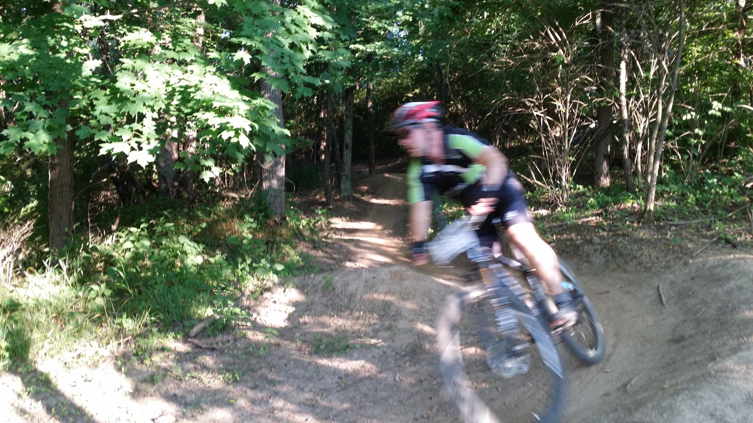 A blurred image of a mountain biker navigating a dirt trail surrounded by trees and greenery, capturing the action and speed of the rider in motion. England Idlewild Mountain Biking Park mountain bike trail.