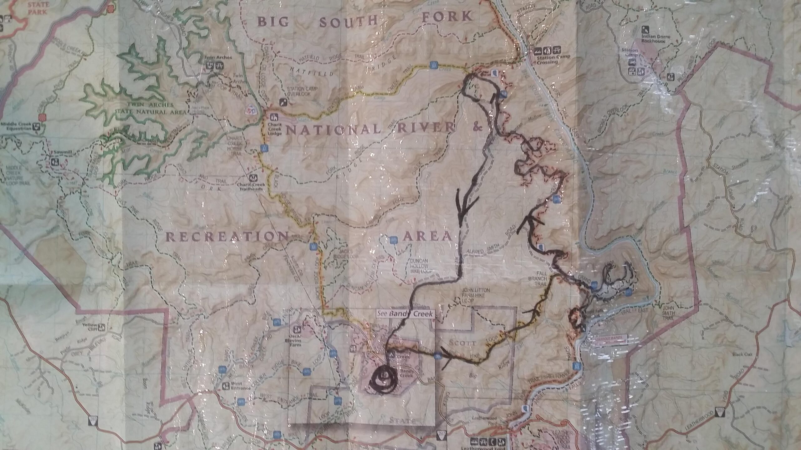 A detailed topographic map of a national recreation area, featuring labeled roads, trails, natural features, and recreational sites. The map includes markings for points of interest, including "Big South Fork" and "Twin Arches State Natural Area," as well as various trails and a waterway. Some sections are highlighted or outlined in black, indicating specific routes or areas of focus. A protective layer of plastic covers the map, suggesting it's been used for outdoor navigation. Big South Fork mountain bike trail.