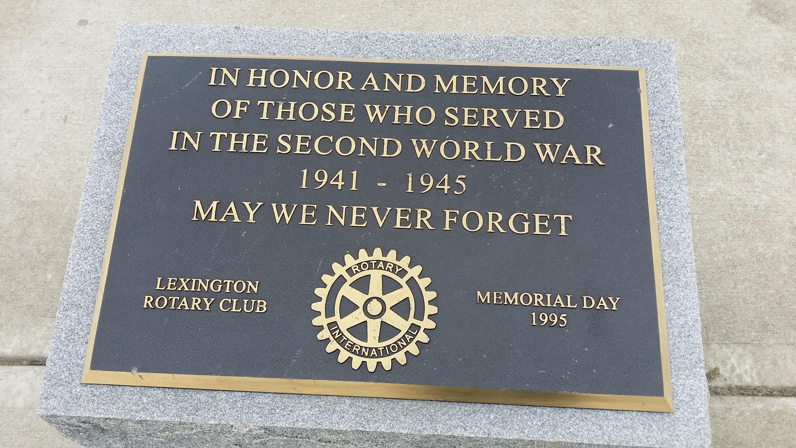 Bronze memorial plaque dedicated to those who served in World War II, inscribed with "In Honor and Memory of Those Who Served in the Second World War 1941 - 1945 May We Never Forget." The plaque is mounted on a stone base and includes the emblem of the Rotary International and references to the Lexington Rotary Club and Memorial Day 1995. Veterans Park mountain bike trail.