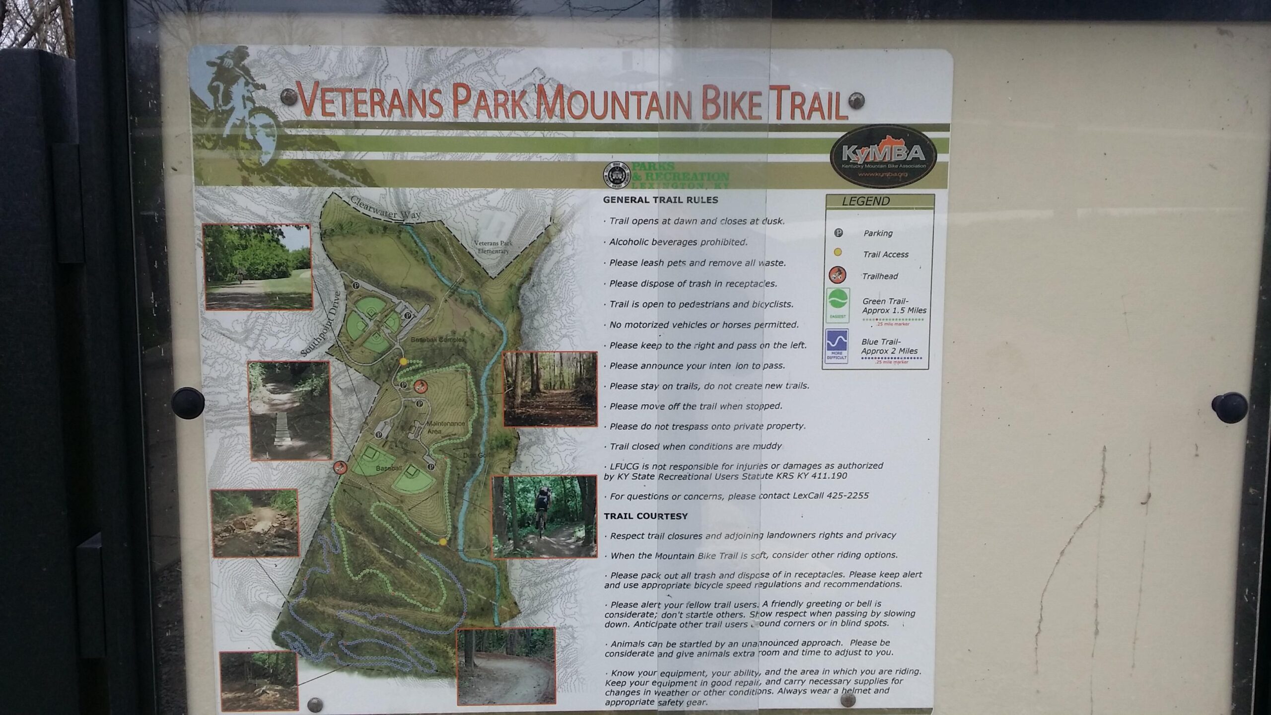 A informational sign for the Veterans Park Mountain Bike Trail features a detailed map showing the trail layout, trail rules, and safety guidelines for cyclists and pedestrians. The sign includes illustrations of the trails marked with different colors, a legend for parking and trail access, and photographs depicting sections of the trail. Descriptions of trail etiquette and restrictions are outlined clearly to ensure visitor safety and enjoyment. Veterans Park mountain bike trail.