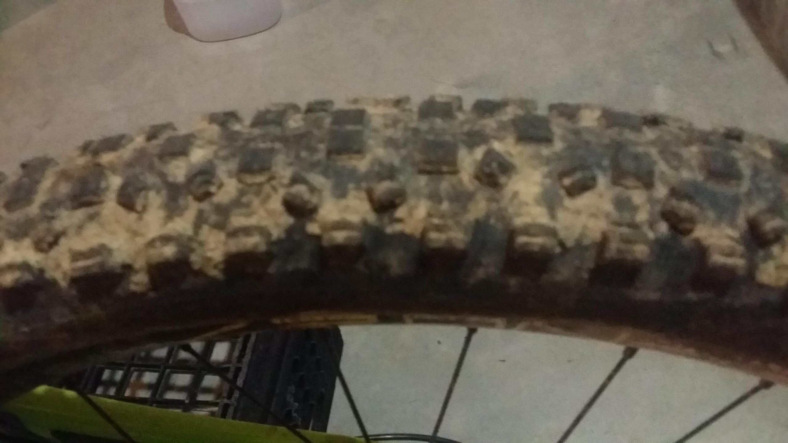 Schwalbe Hans Dampf: Close-up view of a muddy bicycle tire with a rugged tread pattern, set against a concrete background. The tire shows signs of recent use, indicating off-road riding conditions.