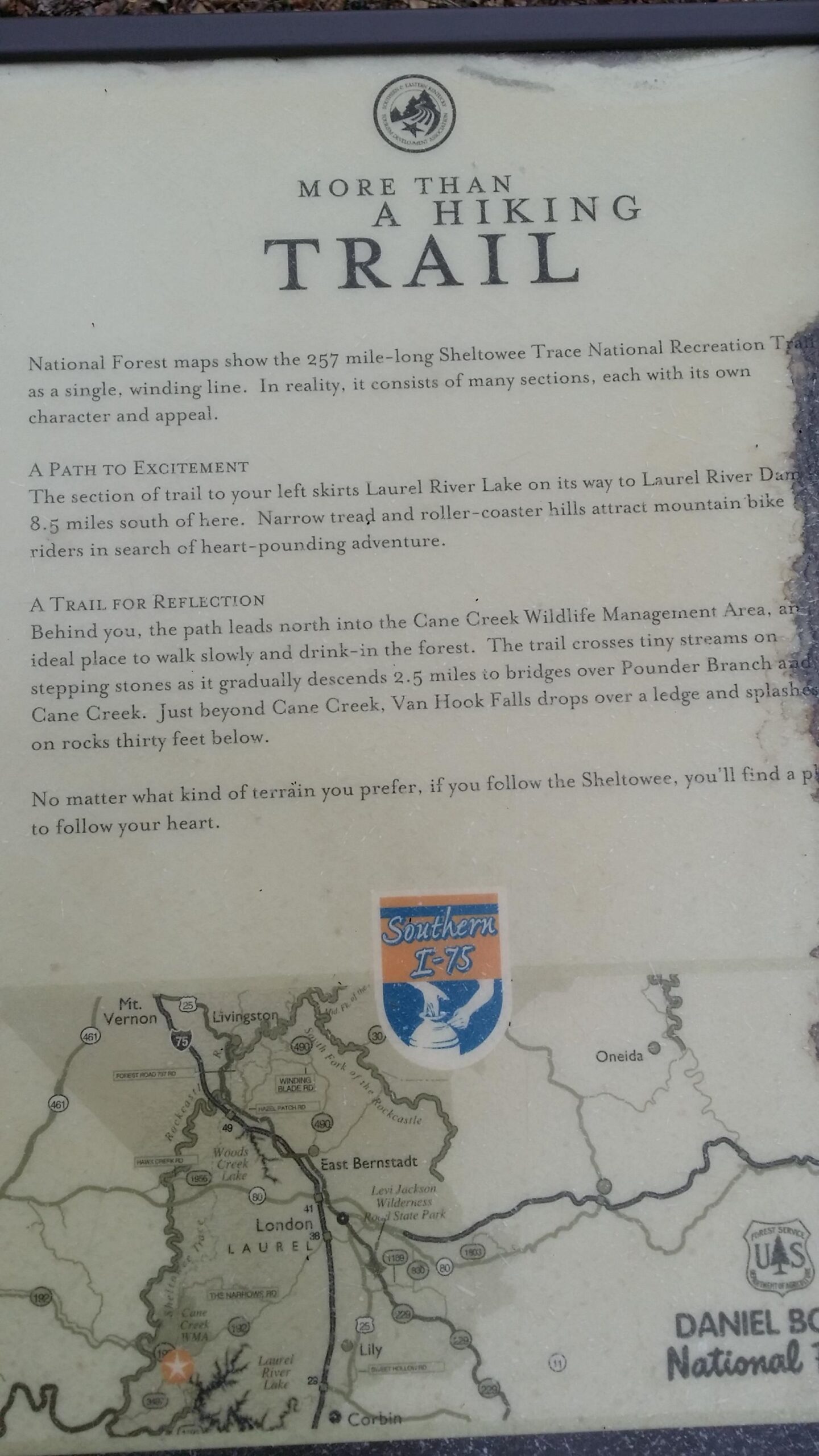 Information sign about the Sheltowee Trace National Recreation Trail, featuring details about the trail's character, nearby attractions like Laurel River Lake and Cane Creek Wildlife Management Area, and advice for hikers on exploring the terrain. The sign includes a map of the surrounding area and notes on the trail's excitement and reflection opportunities. Sheltowee Trace - Laurel Lake Trail mountain bike trail.