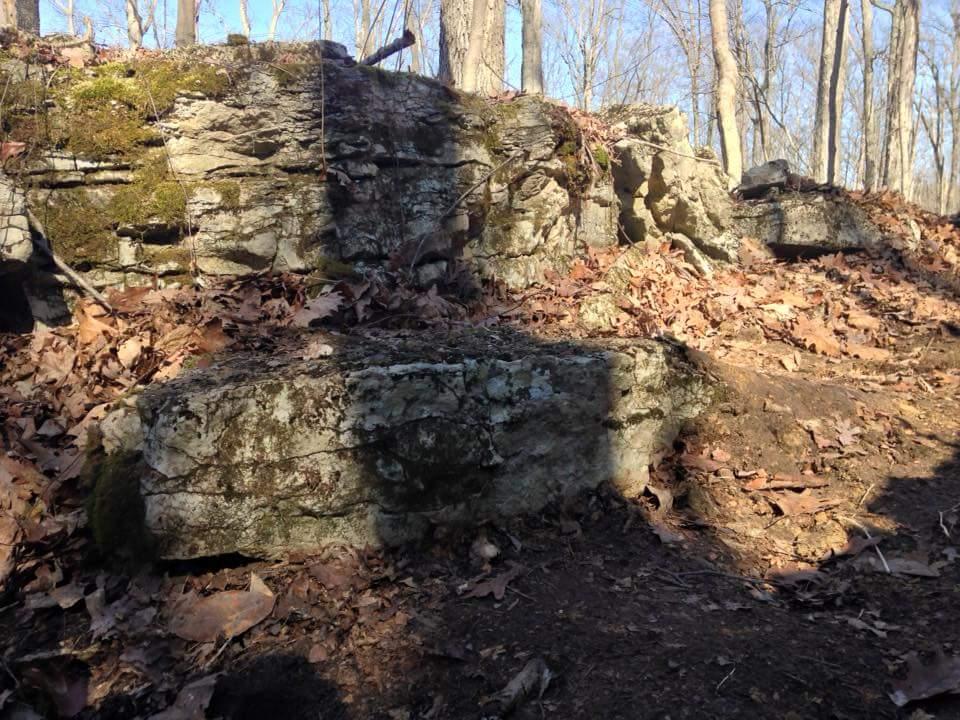 Rock formations covered with moss and surrounded by fallen leaves in a wooded area during the daytime. O'bannon Woods mountain bike trail.