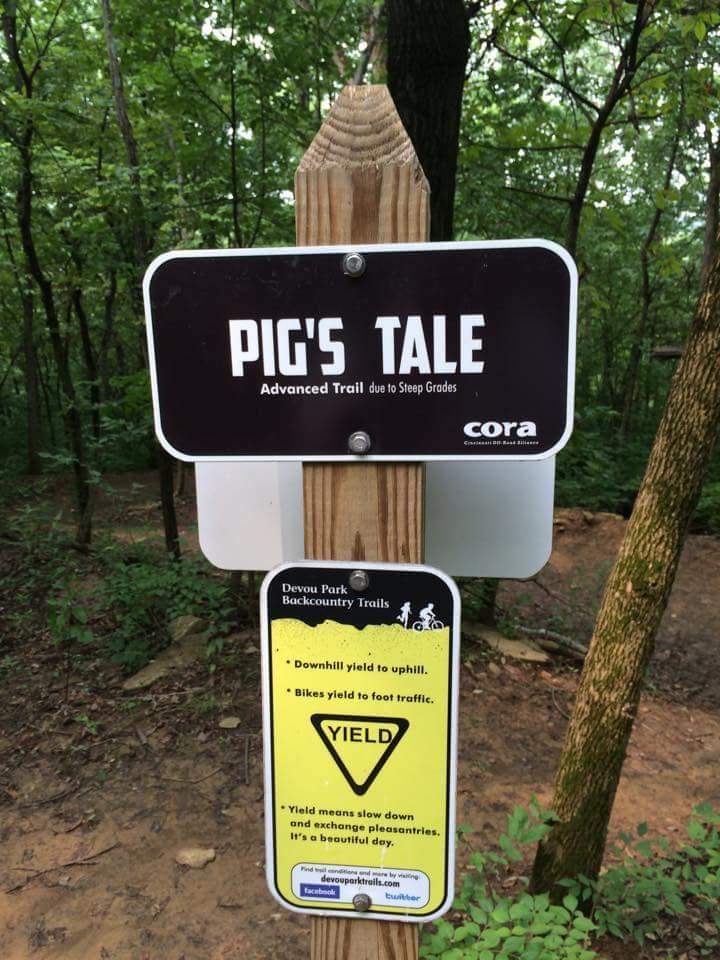 Signpost marking the "Pig's Tale" advanced trail at Devou Park Backcountry Trails, indicating steep grades and providing yield instructions for trail users. Devou Park mountain bike trail.