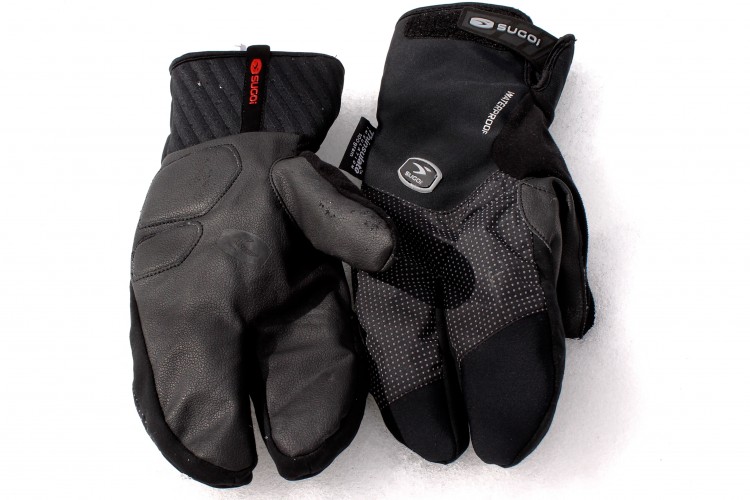 A pair of black winter gloves laid out on a light background. The left glove features a textured leather design, while the right glove combines fabric and leather with a patterned grip. Both gloves have an adjustable cuff and are labeled with the brand "Sugoi," emphasizing their waterproof capabilities.
