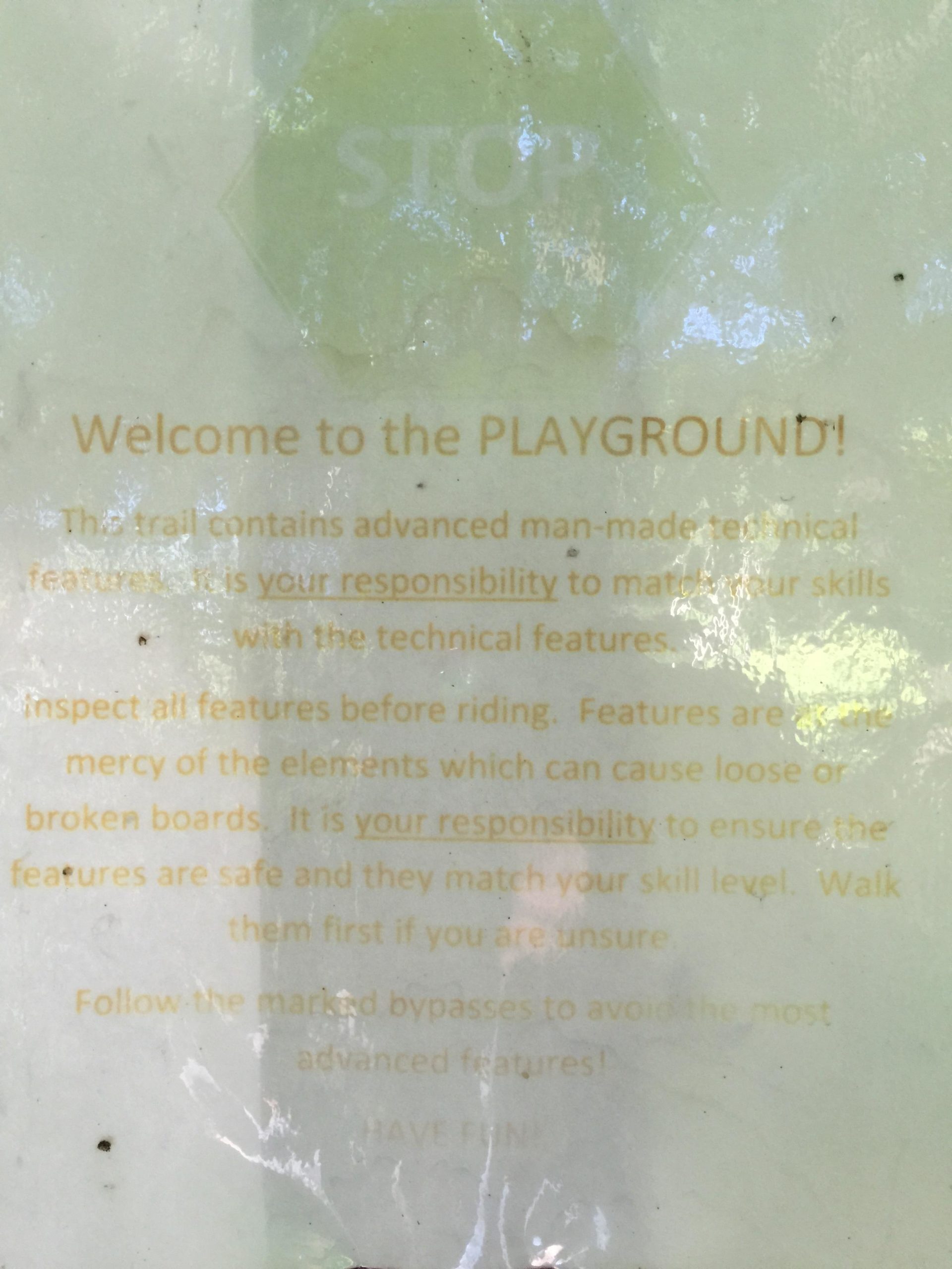 Sign instructing visitors about a playground trail. It emphasizes safety, responsibility, and the importance of matching skills with trail features. The sign includes warnings about inspecting features before use, potential hazards due to weather, and encourages users to follow marked bypasses if unsure. The message concludes with a friendly reminder to have fun. Anderson Park mountain bike trail.