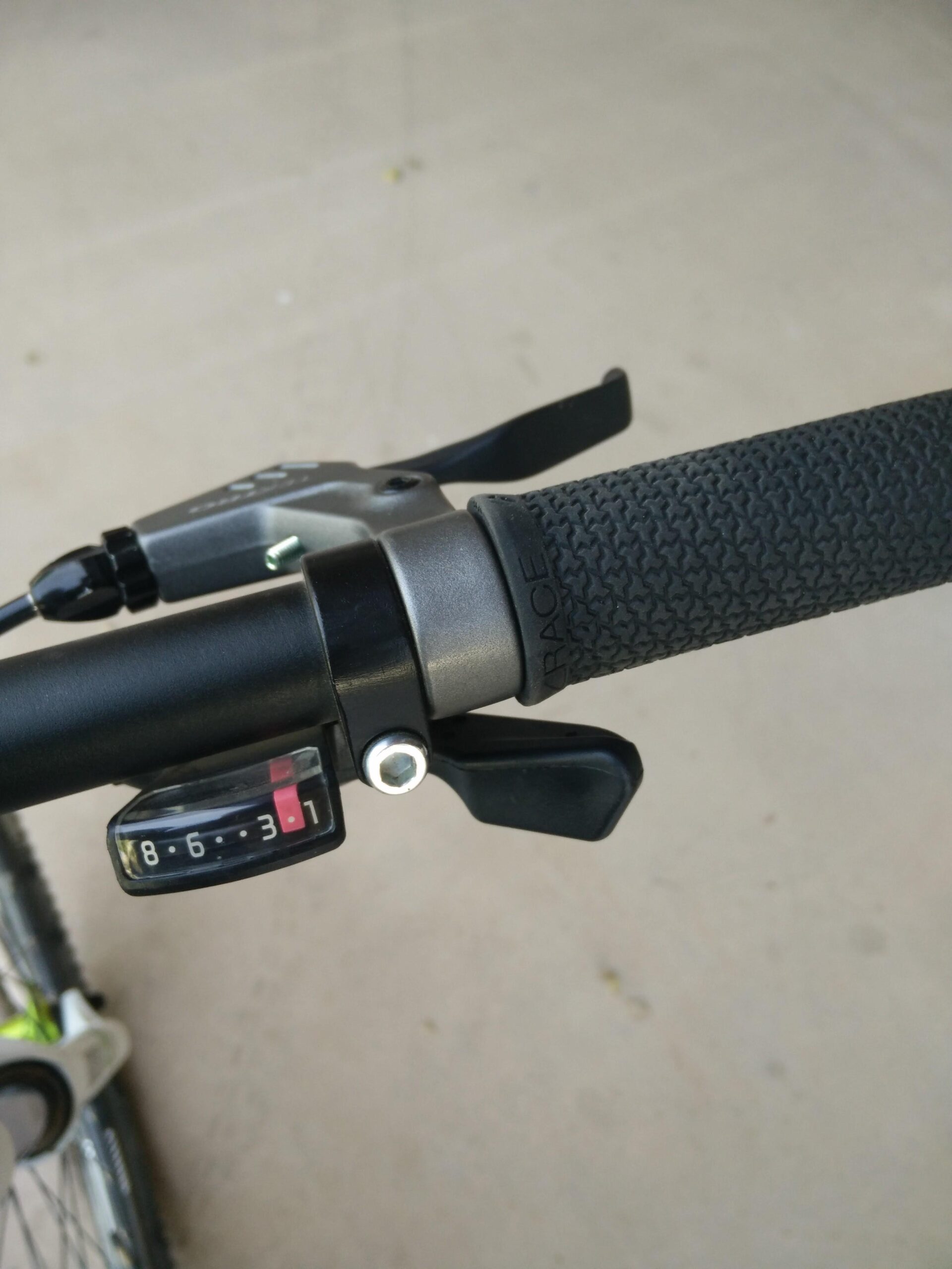 Trek X-Caliber 5: Close-up view of the handlebar of a bicycle, featuring a textured grip, a gear shifter, and a numerical gear indicator displaying "8-6-3-1." The background is a plain, light-colored surface.