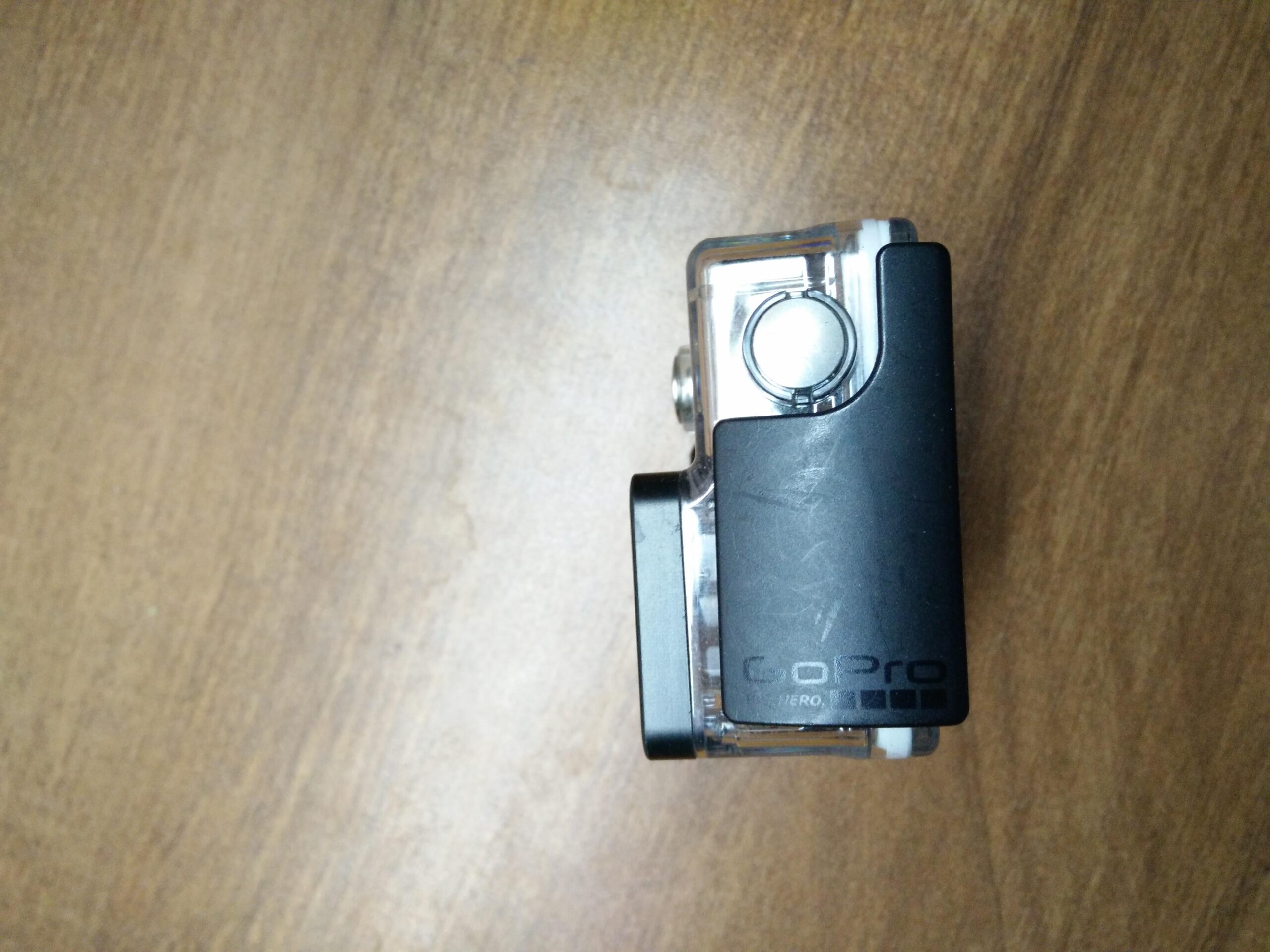 GoPro Hero 3 White Edition: A GoPro camera with a clear housing and black casing, positioned on a wooden surface, showcasing the brand logo and button design.