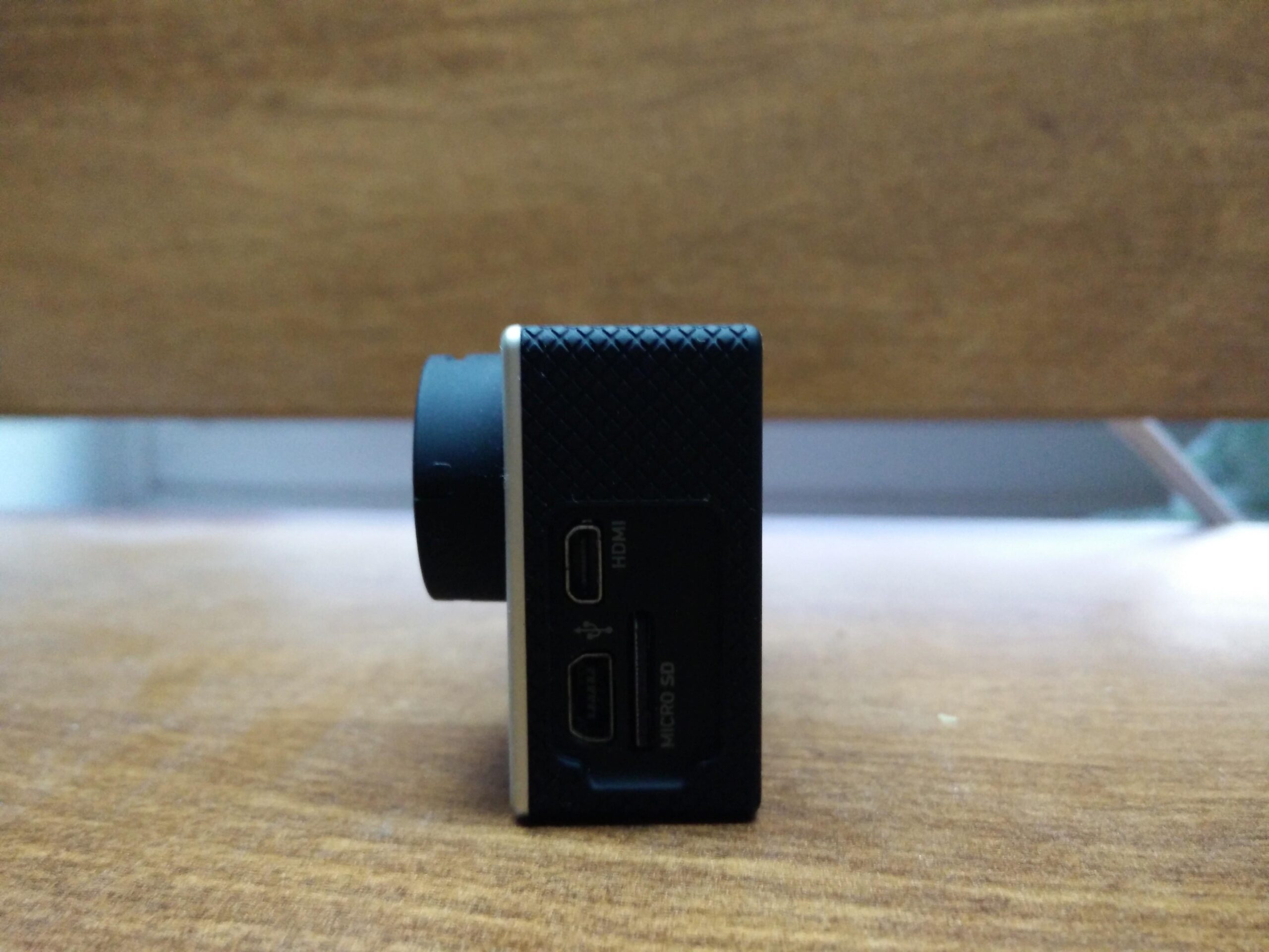 GoPro Hero 3 White Edition: Side view of a small digital camera with visible input ports including HDMI and Micro SD, resting on a wooden surface.