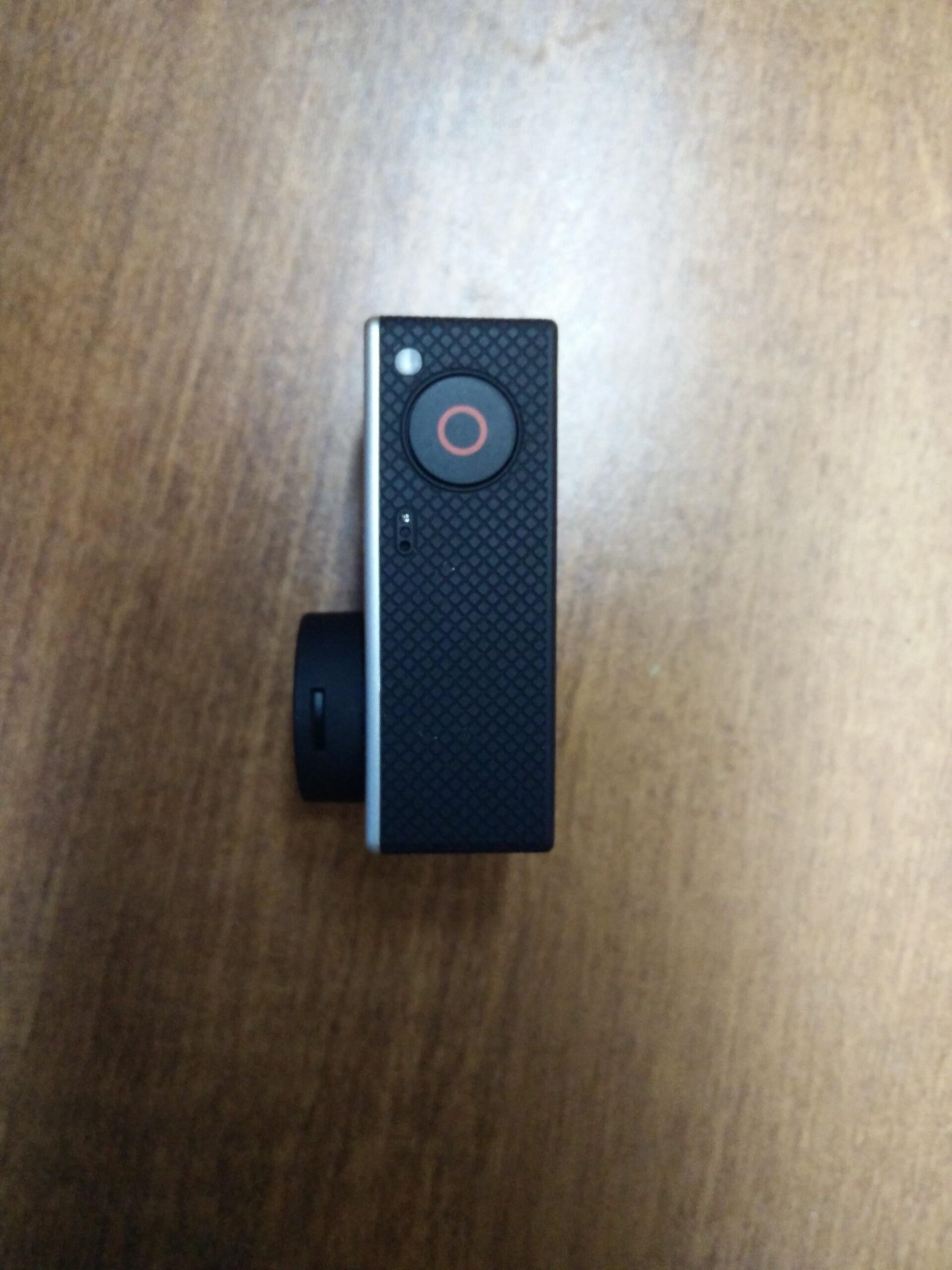 GoPro Hero 3 White Edition: A compact black action camera positioned on a wooden surface, showing the side view with a large red recording button and a small indicator light.