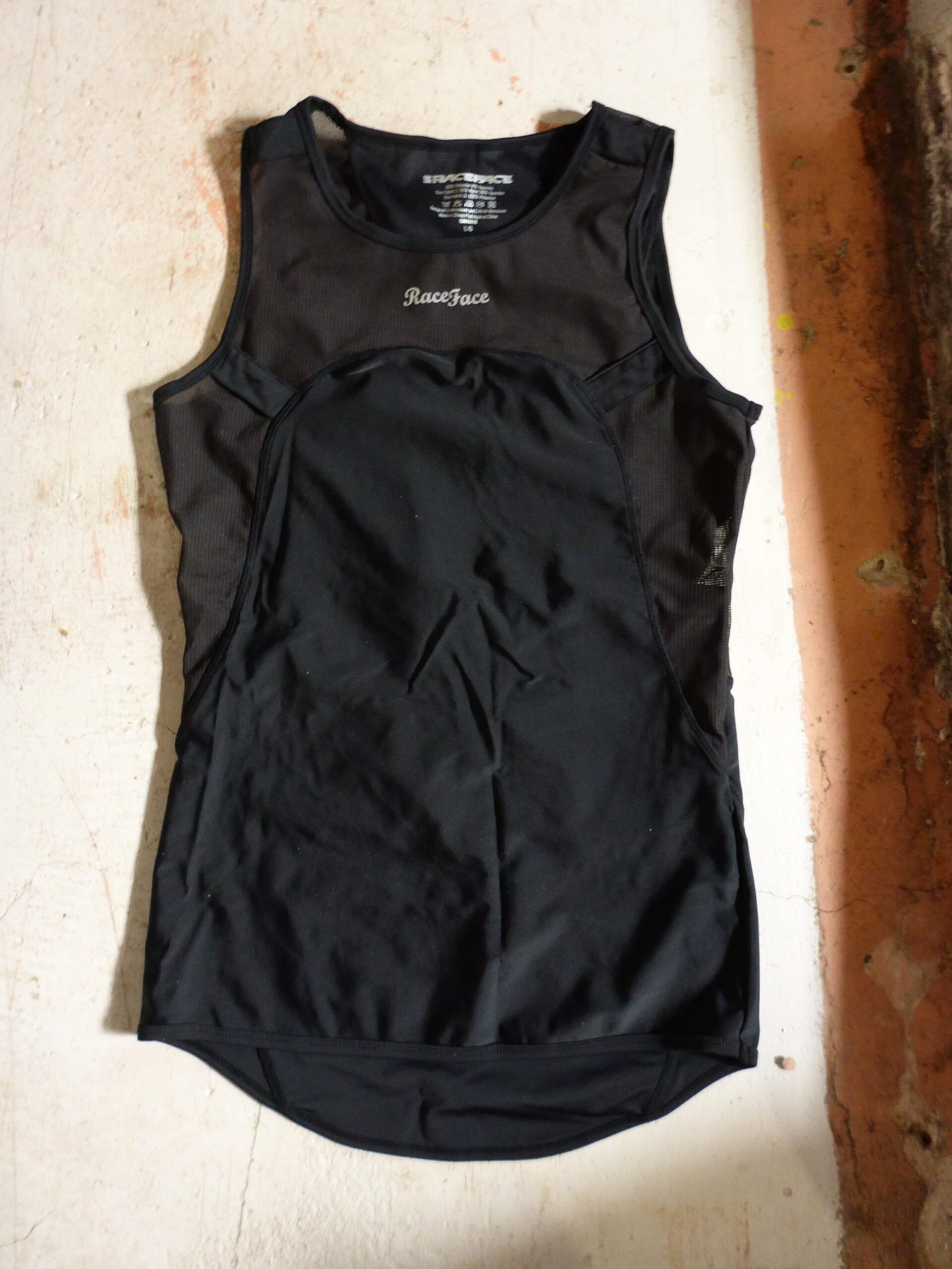 Race Face Stash tank: Black athletic tank top with mesh panels, featuring the logo "RaceFace." The top is laid flat against a textured, light-colored surface.