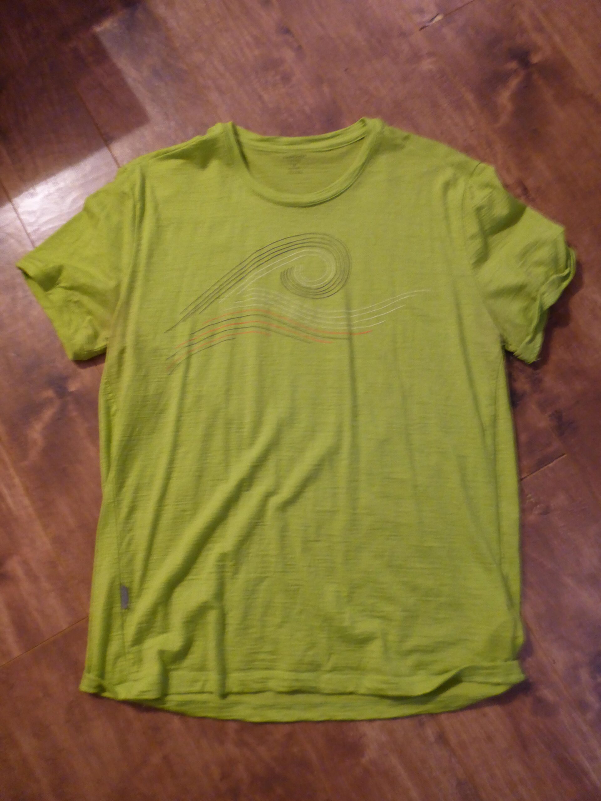Icebreaker t-shirt: A bright green t-shirt laid flat on a wooden floor, featuring a simple wave graphic in various colors.
