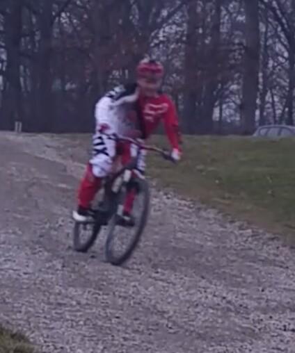 Specialized Hardrock Sport Disc: A cyclist wearing a red and white outfit and helmet is riding a mountain bike on a gravel path. The background features trees, suggesting an outdoor setting.